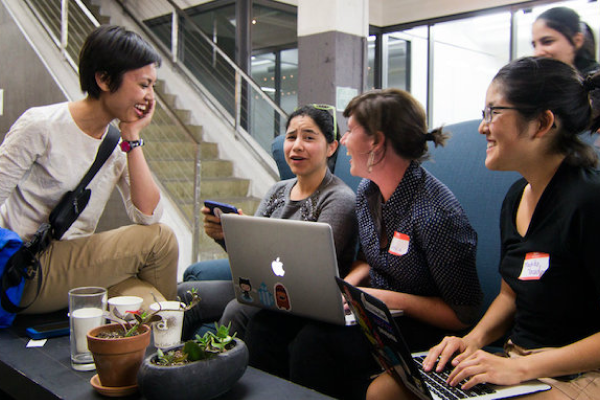 Five women in tech collaborating, engaging in a joyful conversation.